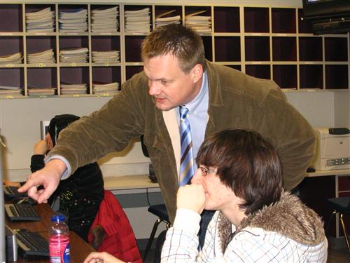 Instructor Sherm Iversen pointing at a computer monitor as he helps a student 